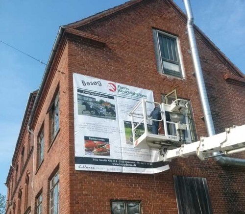 Det store banner for Fyens Væddeløbsbane er ved at blive monteret på gakven på ejendommen Vesterbro 116.